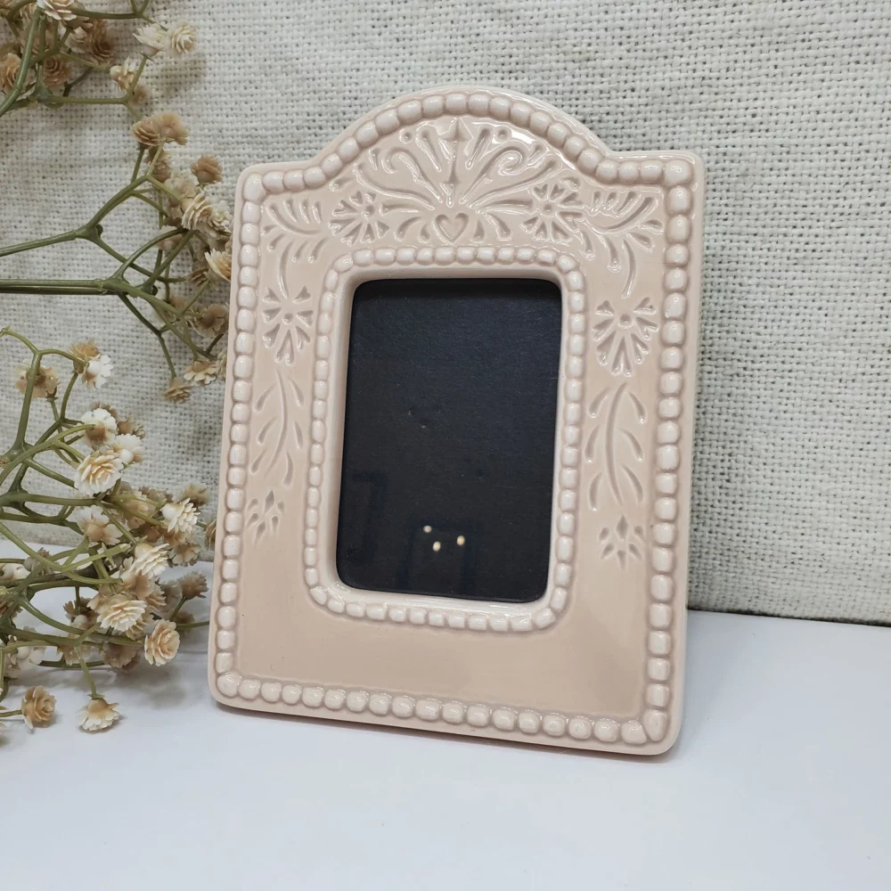 Pastel pink coloured ceramic picture frame beside some decorative flowers