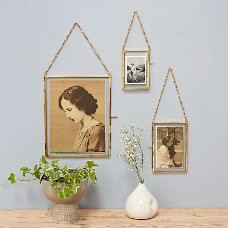 Hanging photo frames on top of a console table with a flower vase and planter on it