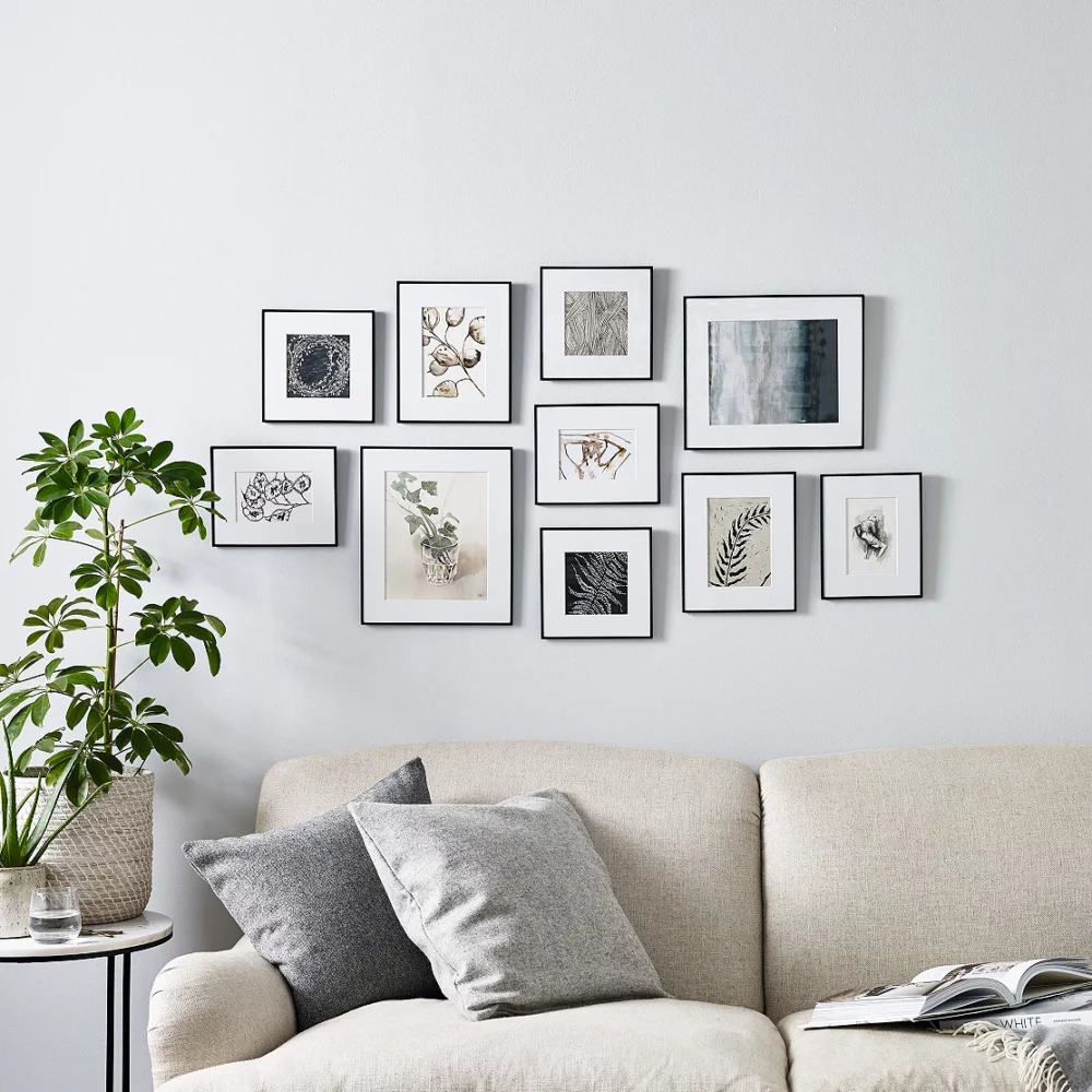 White mat collage photo frames on the walls of the living room along with a sofa set with cushions on them and an indoor plant on the side table