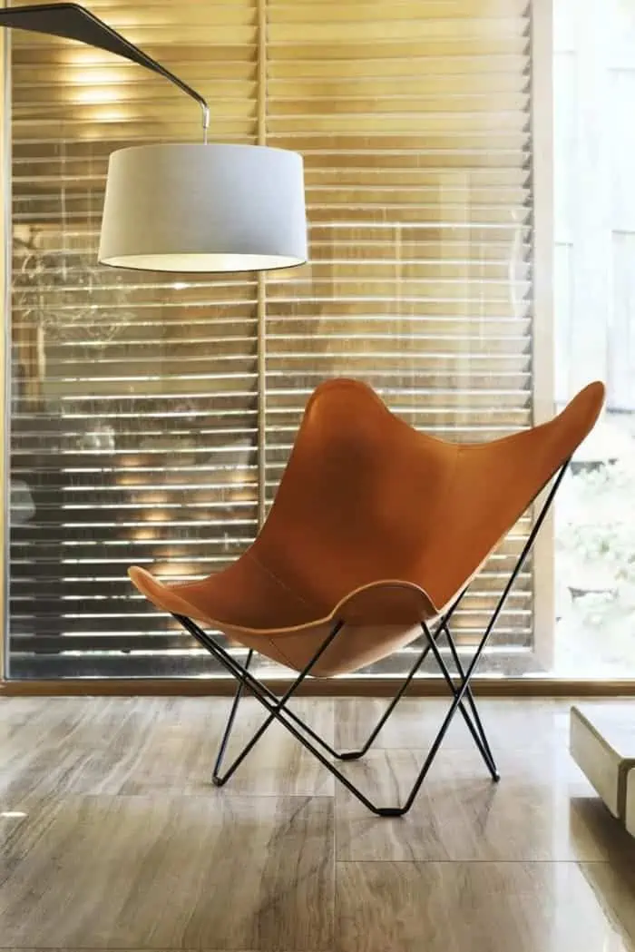 brown leather folding-chair with metal legs placed in a home setting with wooden flooring and a lamp