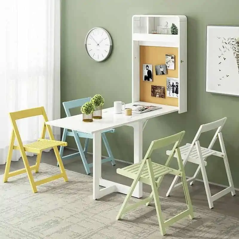 A white foldable dining table set with 4 chairs in colours white, light blue, light green, and yellow, in a room with green walls