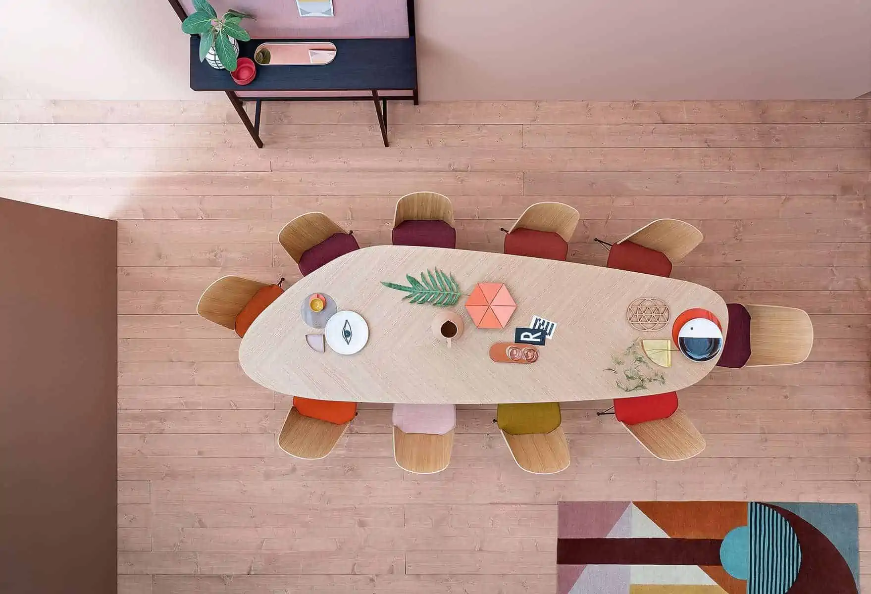 A freeform 10 seater dining dining table set with multicolour cushions, room with wooden floor captured from the ceiling