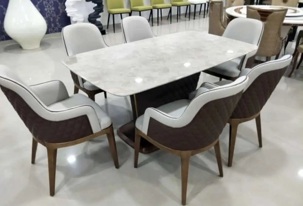 white glossy marble top dining table set 6 seater, with rounded corners, chairs with white and brown seating with wooden legs, in a showroom setting