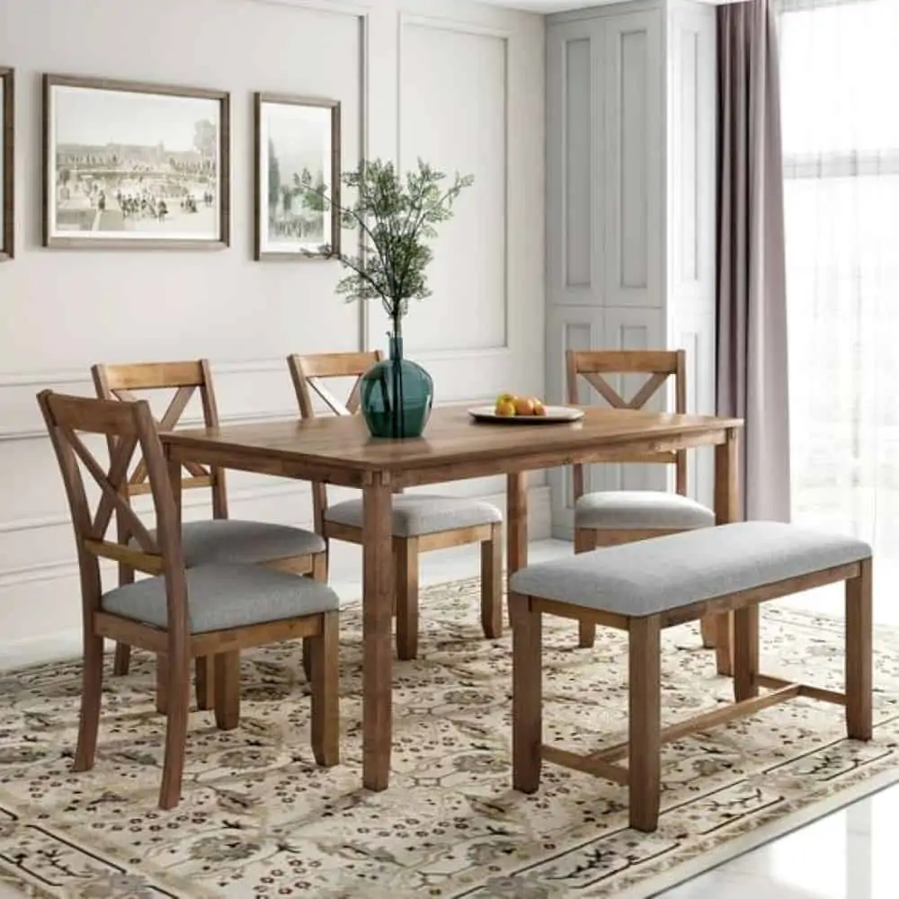 Light brown mdf dining table set, with chairs and a bench, with light gray seats, in a white walled dining room with wall hangings and a rug