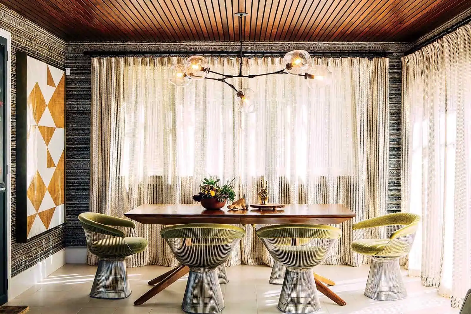 Classy Platner Armchair dining set with metallic frame and a padded seat with a pattern wall painting and metallic finish curtains.