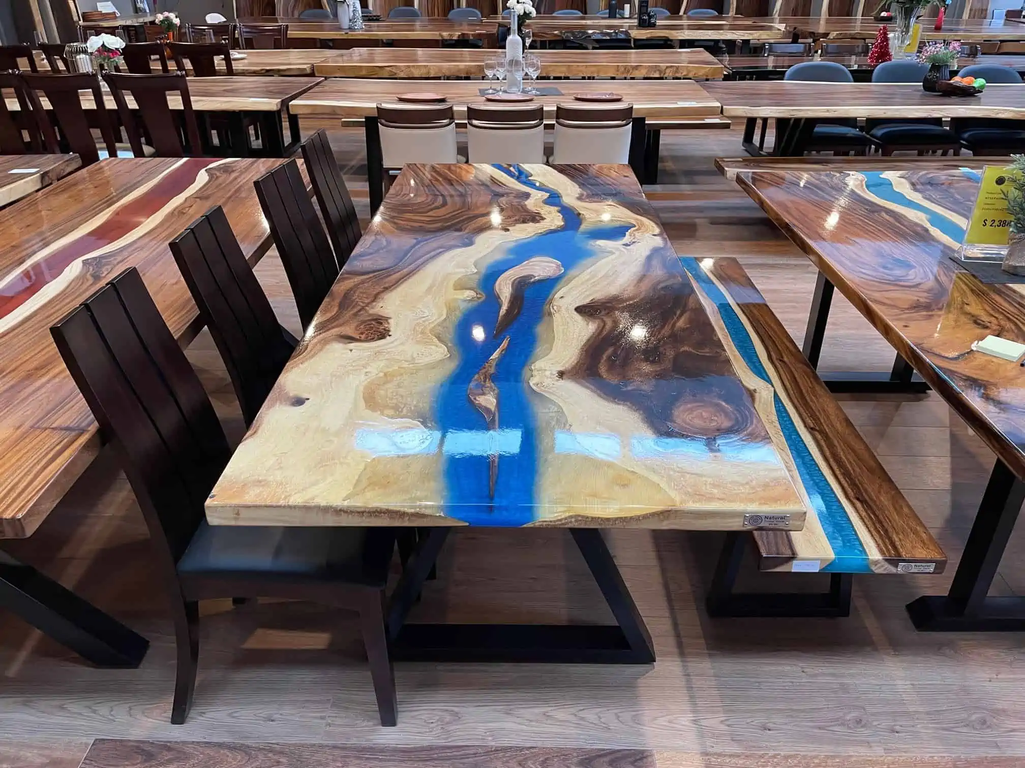 Epoxy resin top dining table with blue and wood colours, with a wooden frame, and dark brown wooden chairs, in a showroom