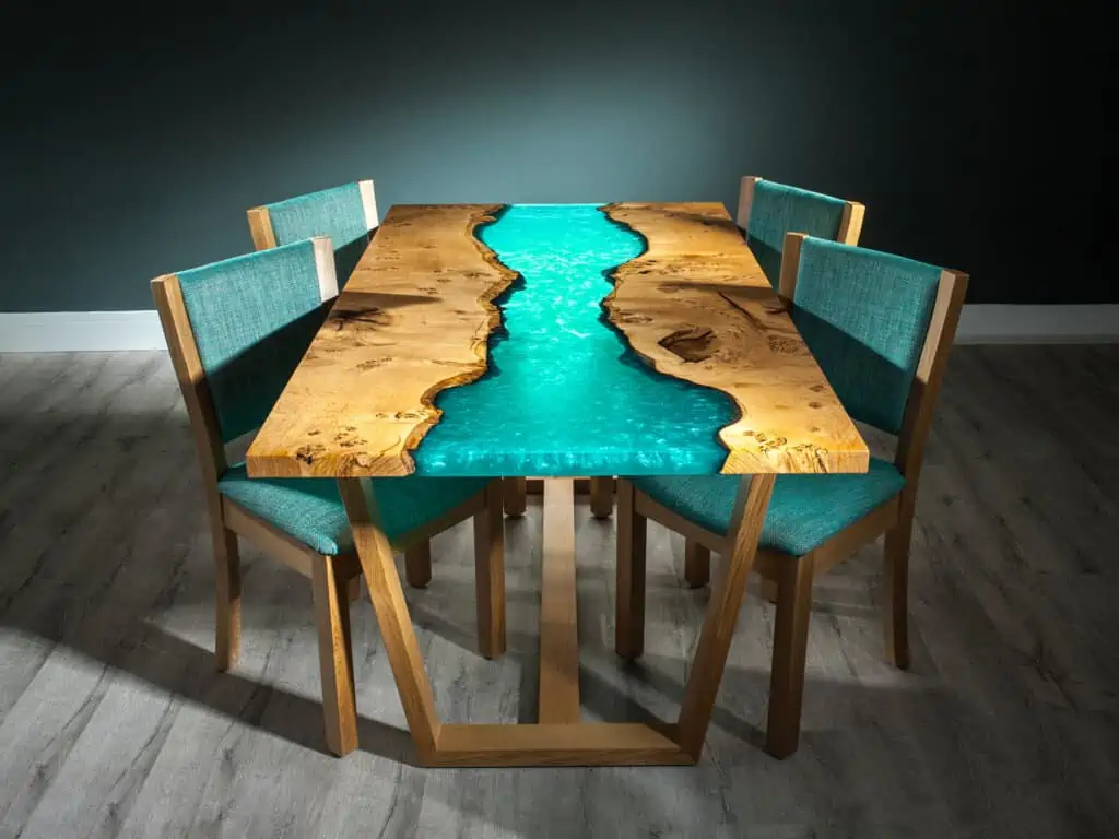light blue and wood coloured resin top rectangle 4 seater dining table with blue chairs and wooden frame, in a room with dark green walls