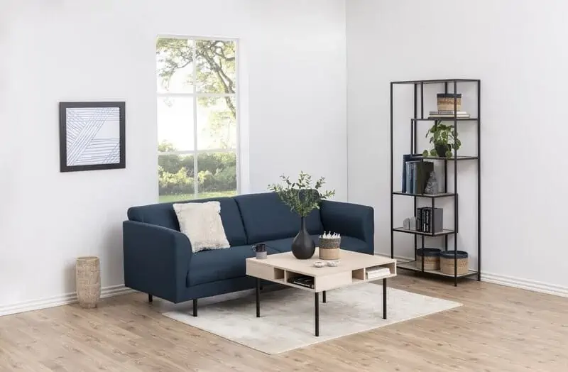 living room with sofa set, study table, window, wall hanging, off white walls, wood coloured flooring, bookshelf in the corner