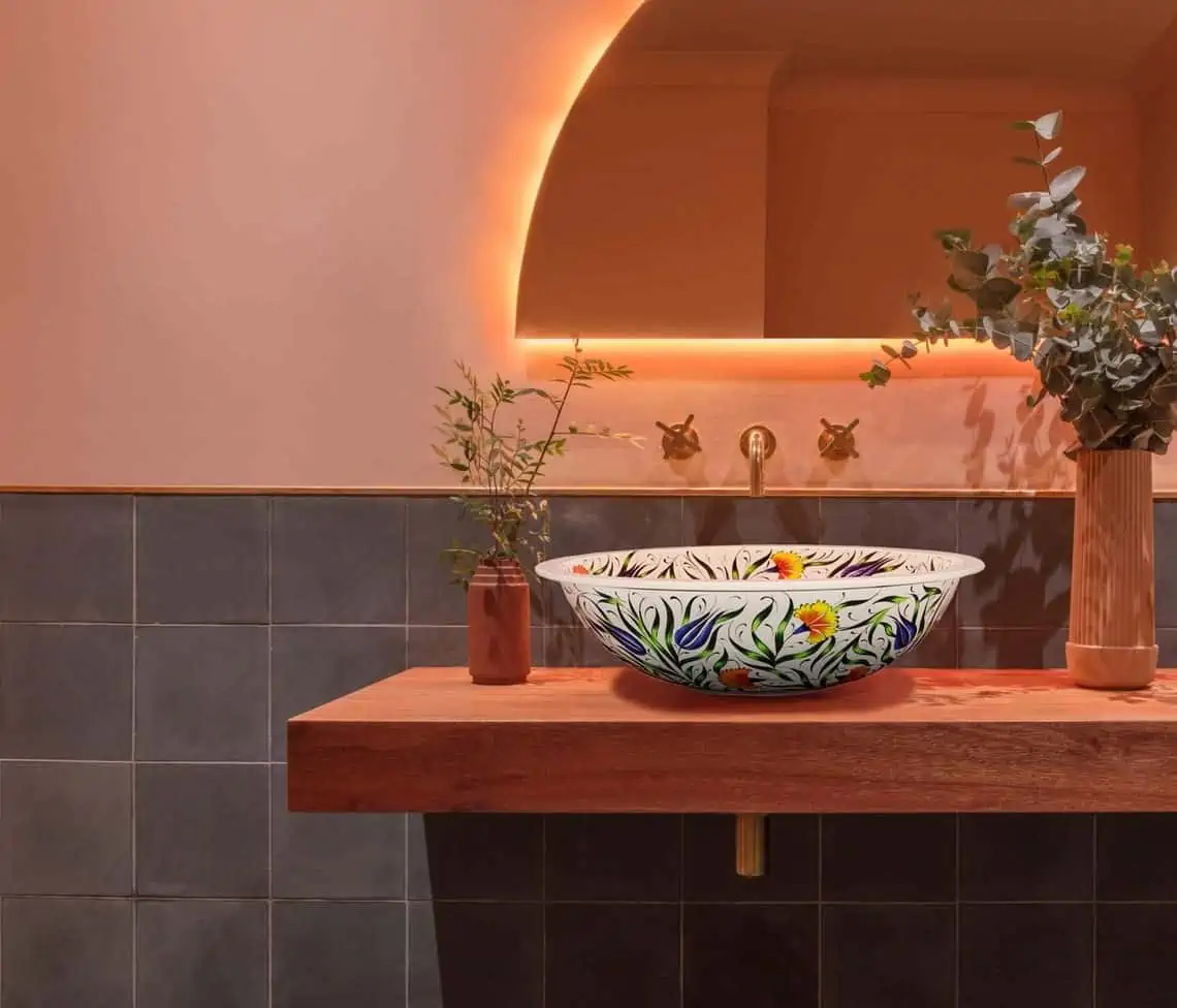 colourful washbasin in a bathroom with a mirror with light strips and an indoor plant