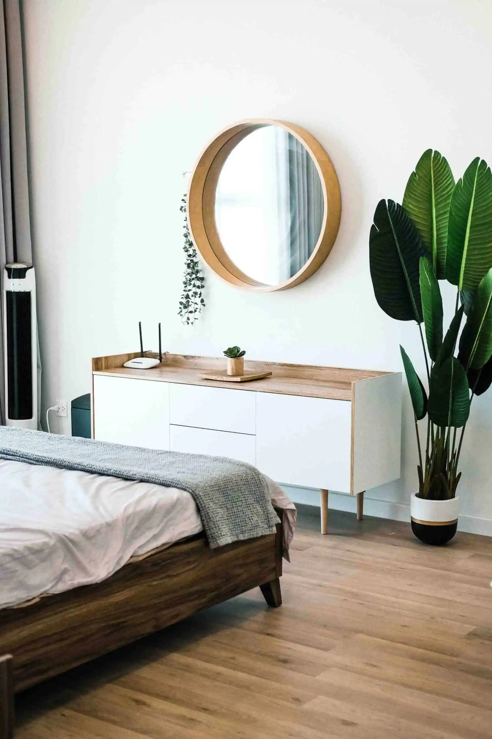 minimalistic mirror on a white wall with indoor plant and a bed in a bedroom
