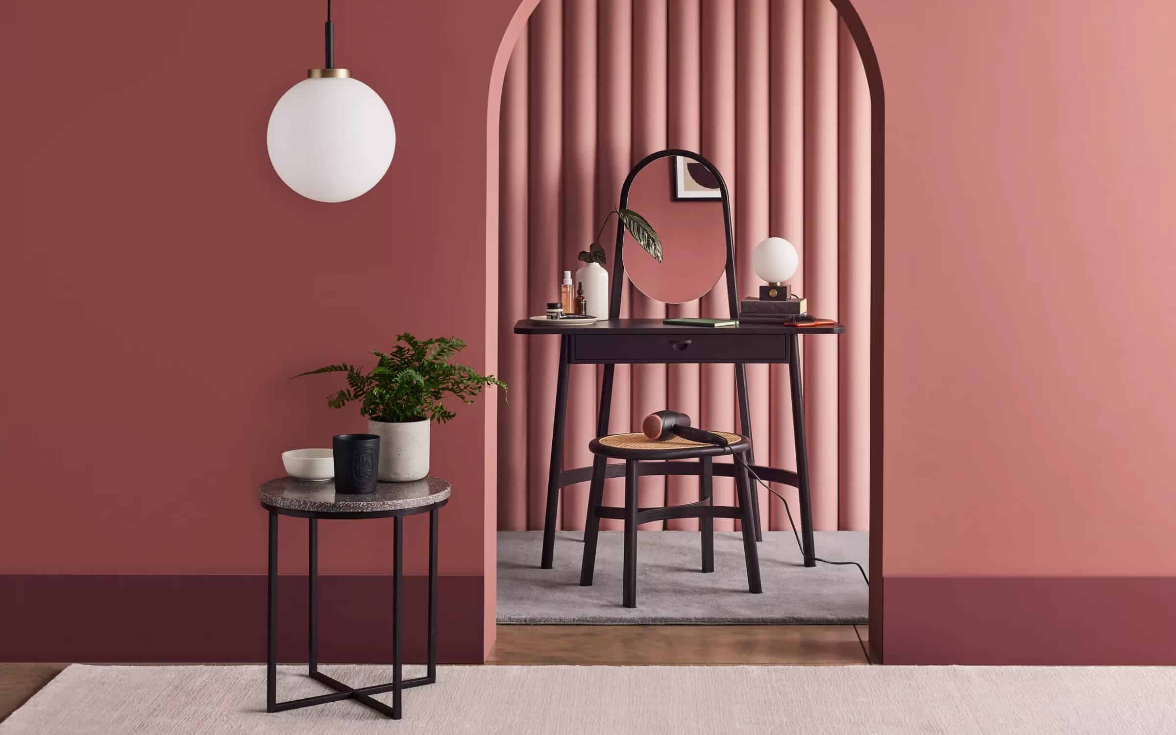 A pretty black color dressing table design with a oval mirror, minimum storage space, and a matching stool, in a pink room.