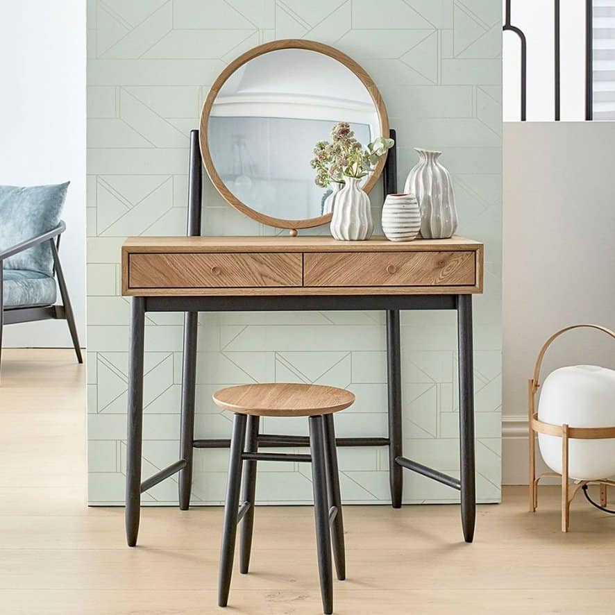 A pretty dresser with a round mirror, minimum storage space, and a matching stool, in a white room.
