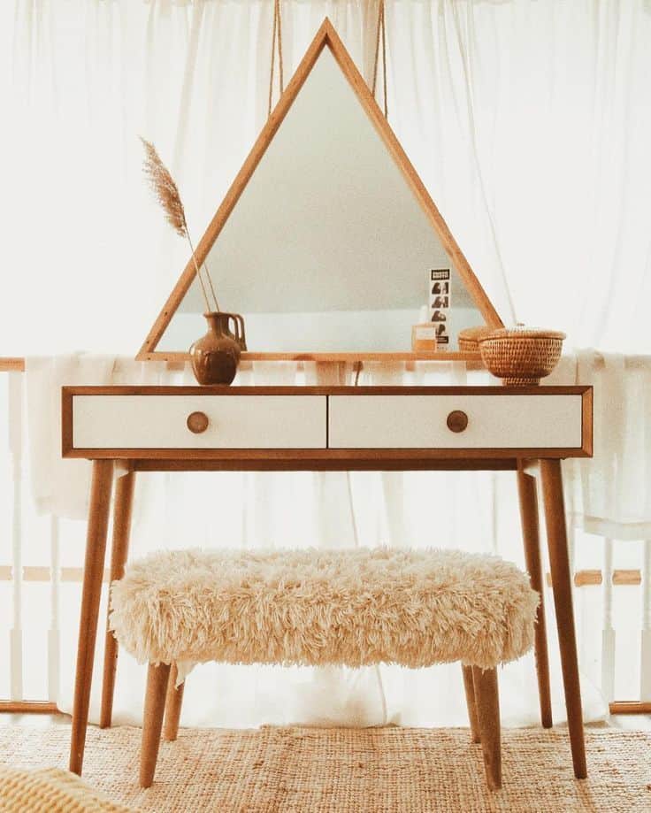 A stylish wooden dresser with triangular mirror, storage drawers, and a matching stool, in a white room.
