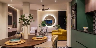living room with brown table and chair and yellow sofa, mirror with light strip and a fan, home by the best and top interior designers in chennai