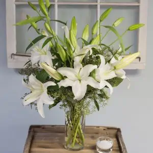 White lily flowers in a glass vase with green foilage