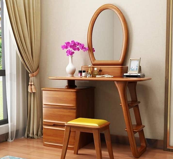 A graceful wooden dresser with a oval mirror, good storage space, and a matching stool, in a white room.