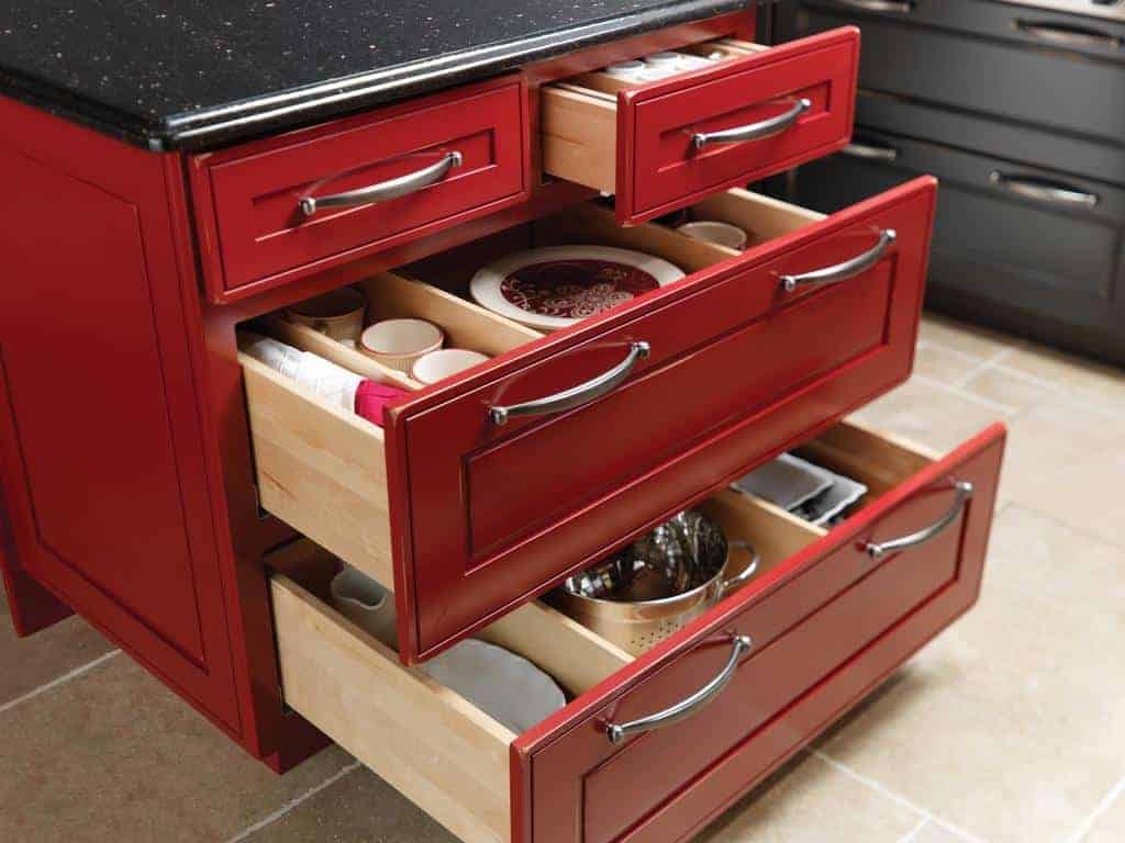 A red-colored tandembox of a cabinetry displaying some utensils and crockery.