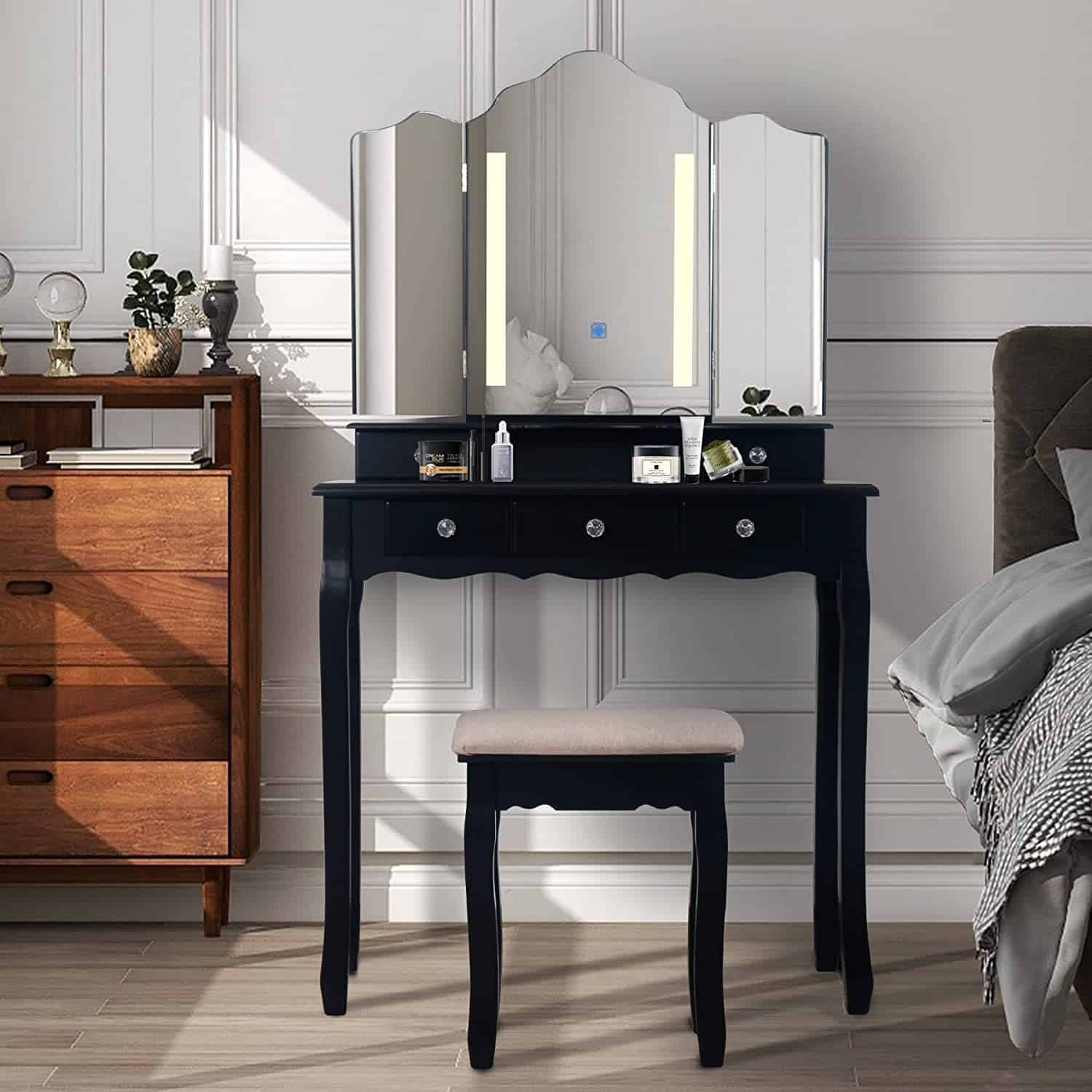 A beautiful, wooden, black-colored dressing table design with 3-fold mirrors, minimum storage space, and a matching stool, in a white room.