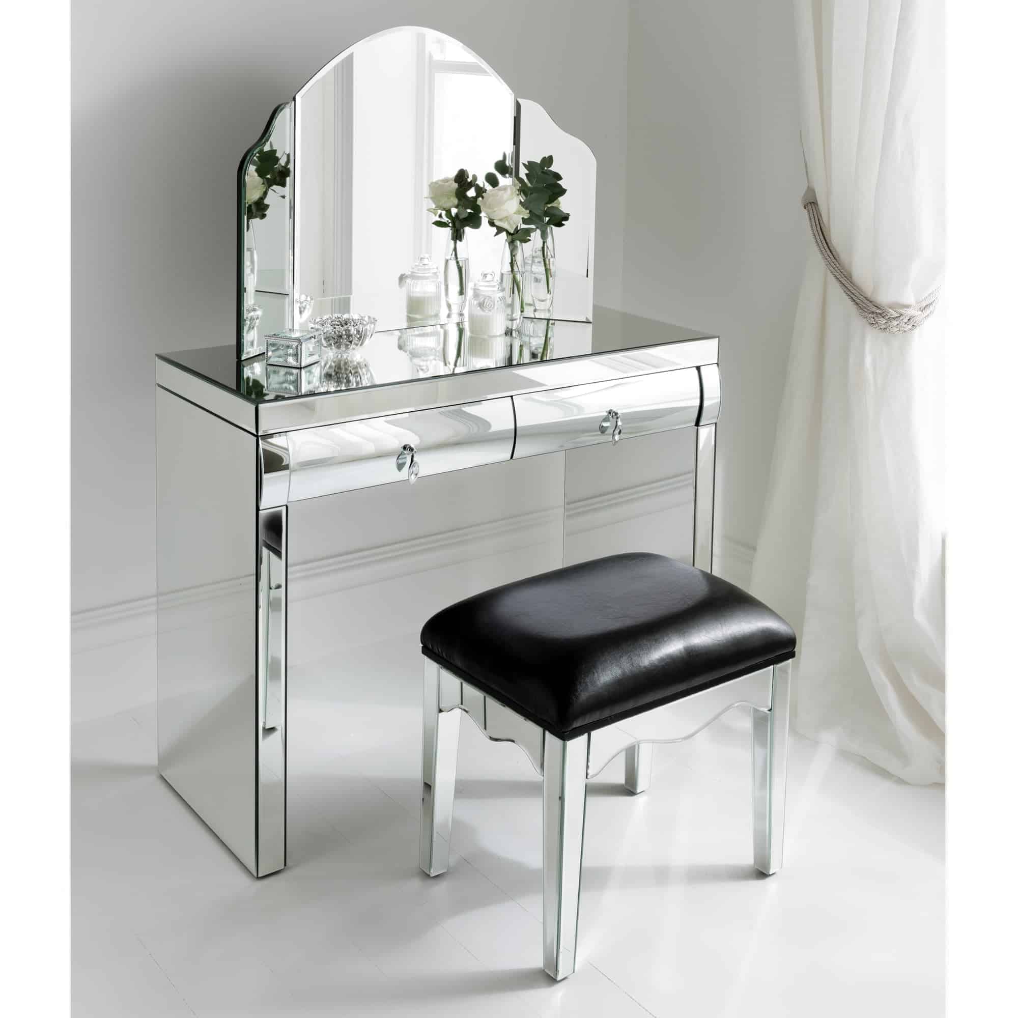A stylish glass dressing table with a matching stool, kept in a white bedroom with no decor.