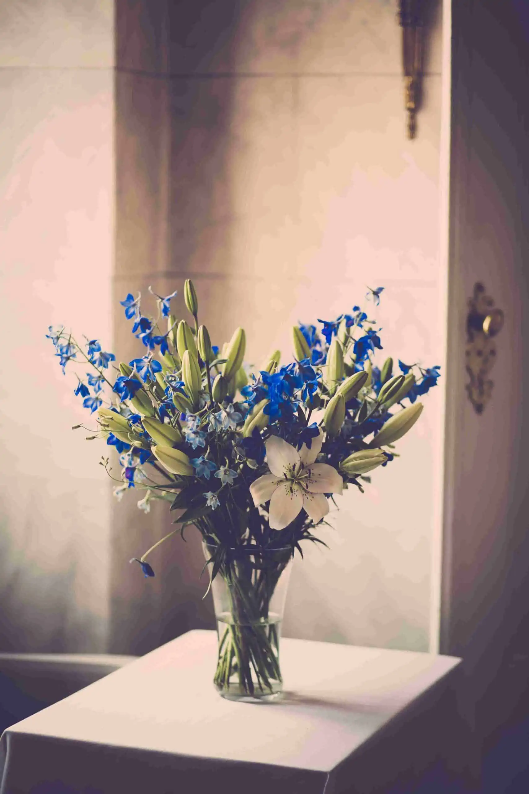 White lily flowers in a glass vase with green foilage