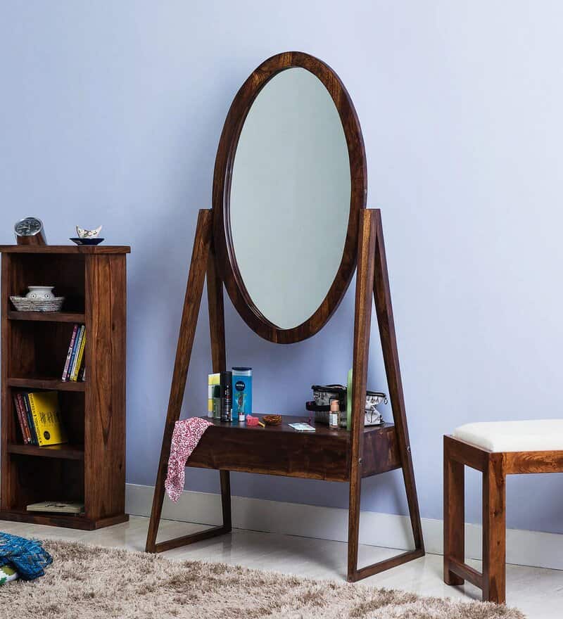 A unique dresser with oval mirror and a hanging shelf, kept in a blue-coloured bedroom with other furniture.