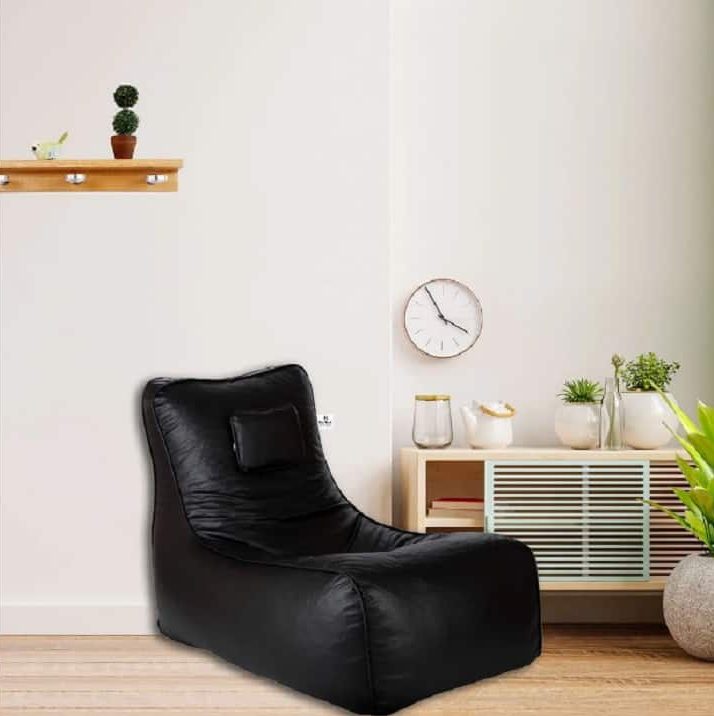 Black jumbo bean bag place near a small cabinet with a wall clock and wooden flooring