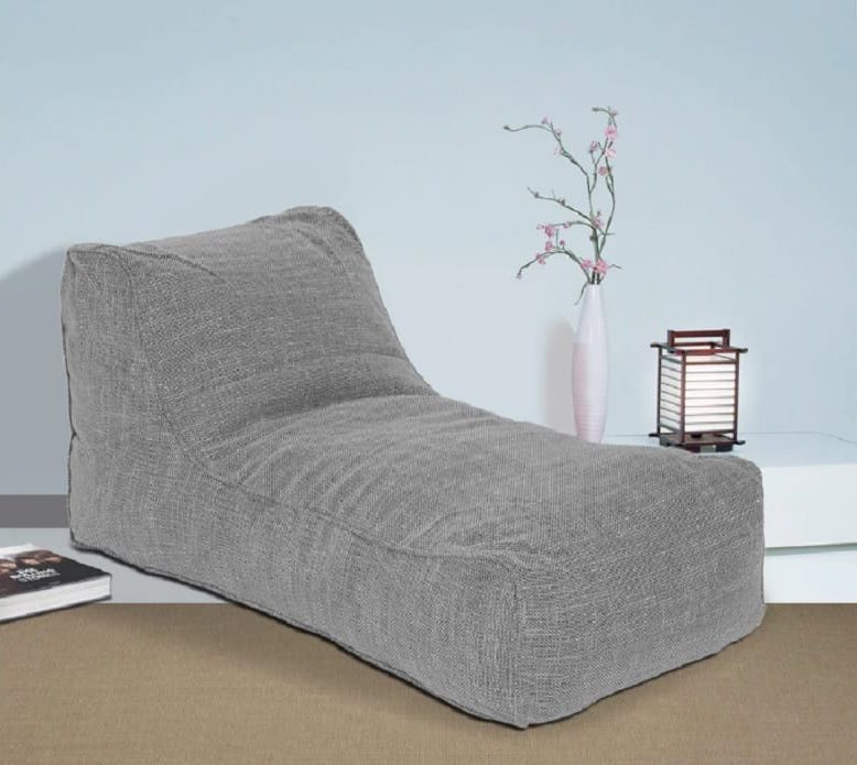 comfortable grey lounger chair placed near a vase and a floor lamp