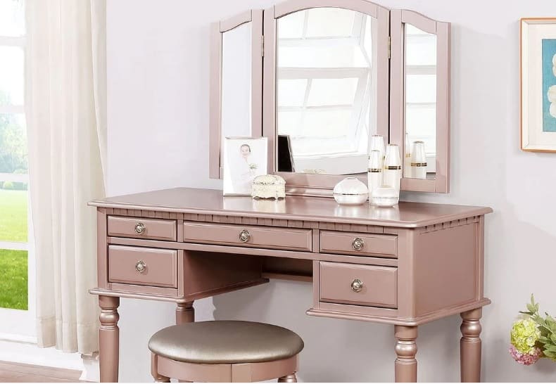 blush pink vintage vanity with a tri-fold mirror and metallic knobs