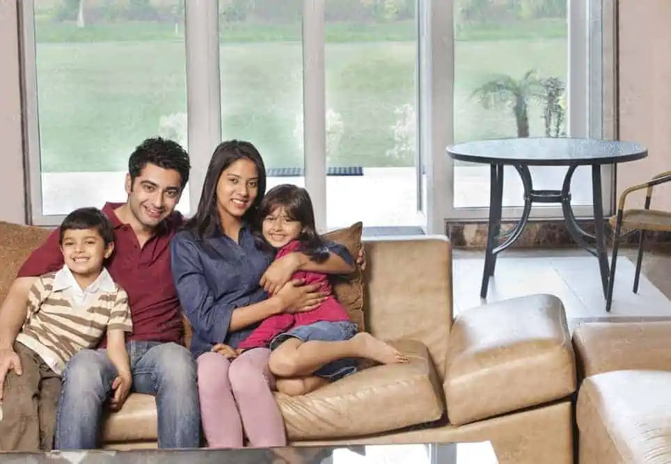 a family with 2 kids and parents sitting on a couch sofa with glass doors and windows in the background