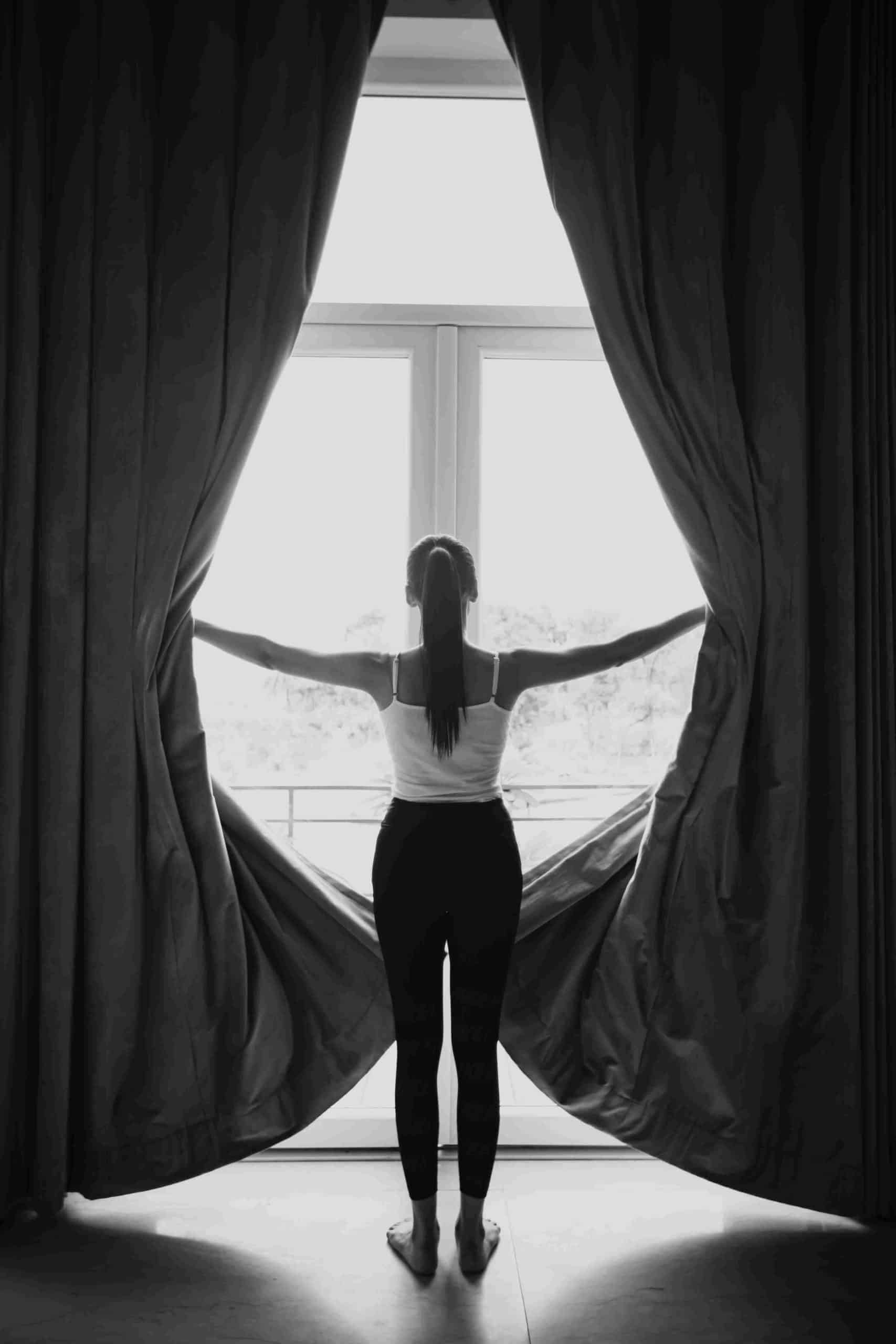 a girl standing in front of her glass and upvc fenestration drawing the curtains away