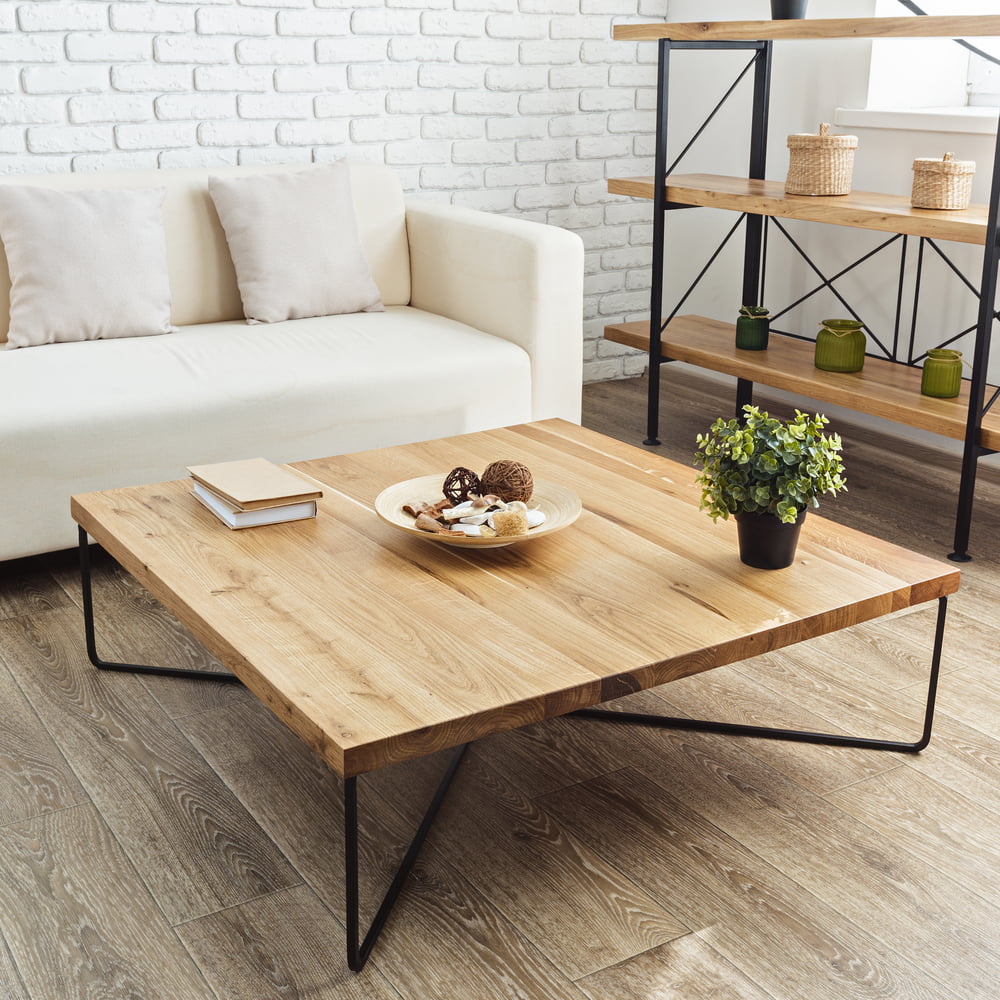 square shaped rustic coffee table in a living room, made of reclaimed wood ,with a metal base, beige sofa, a wooden and metal shelf, books, plant, minimal living room, wooden lamination on floor, white walls