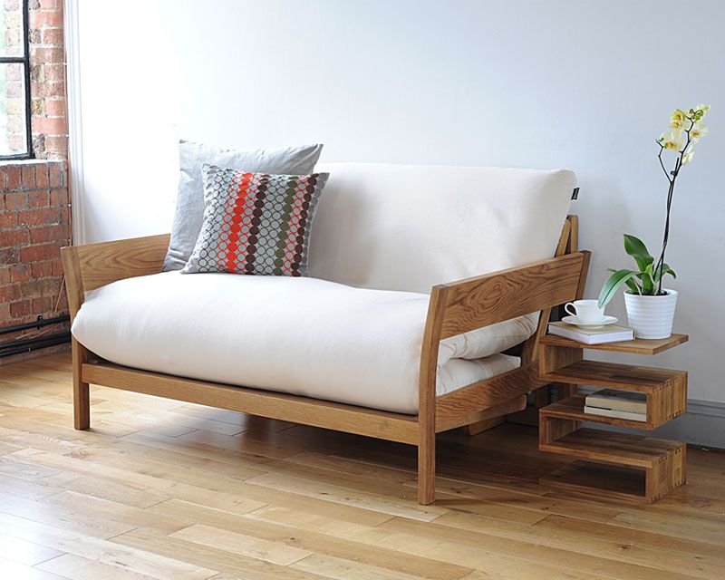 beige coloured compact two-seater futon, wooden frame, cushions, white walls, side table with storage, wooden laminated floor