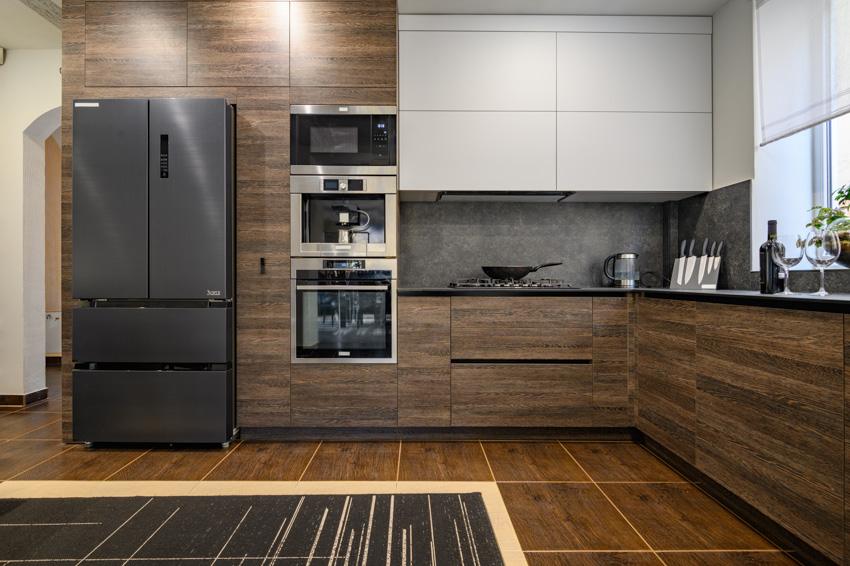 brown kitchen with wooden floors, fridge, appliances and white cupboards
