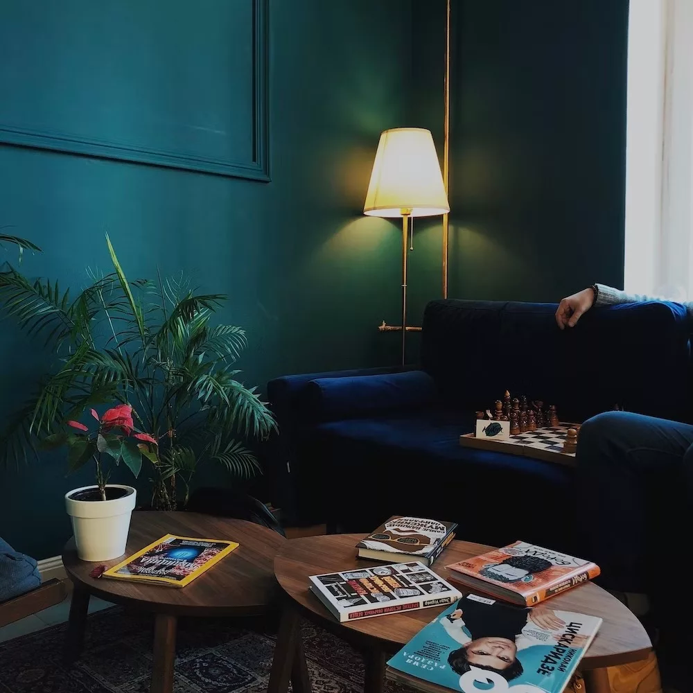 living room decor, brown wooden coffee table, ceramic indoor planter placed on the table, table lamp, blue velvet sofa, books on the table