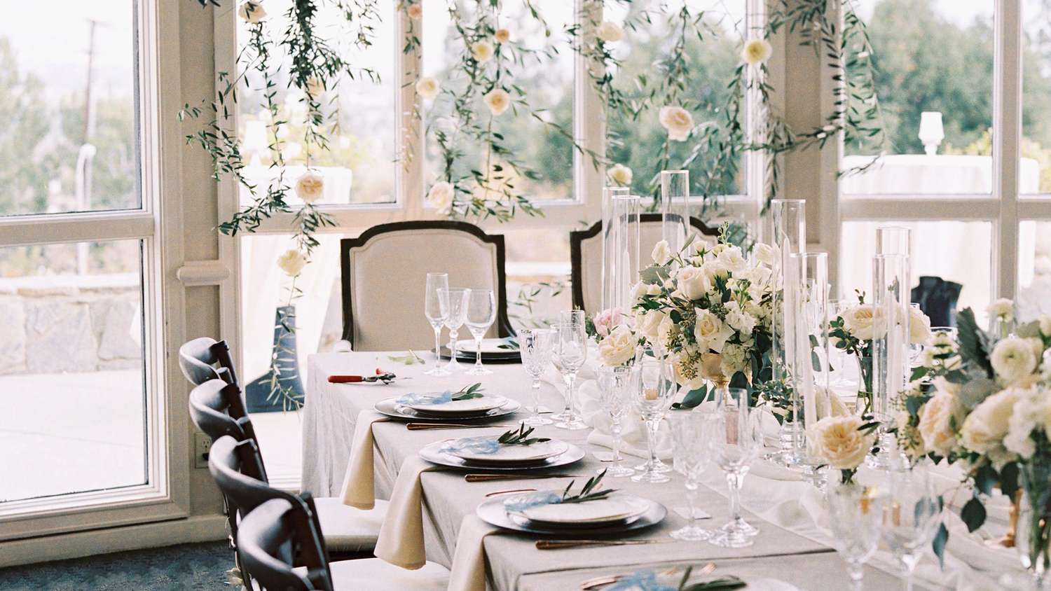 white dinner table setting in a hall with chair, table, floral decorations, plates, cutlery and napkins
