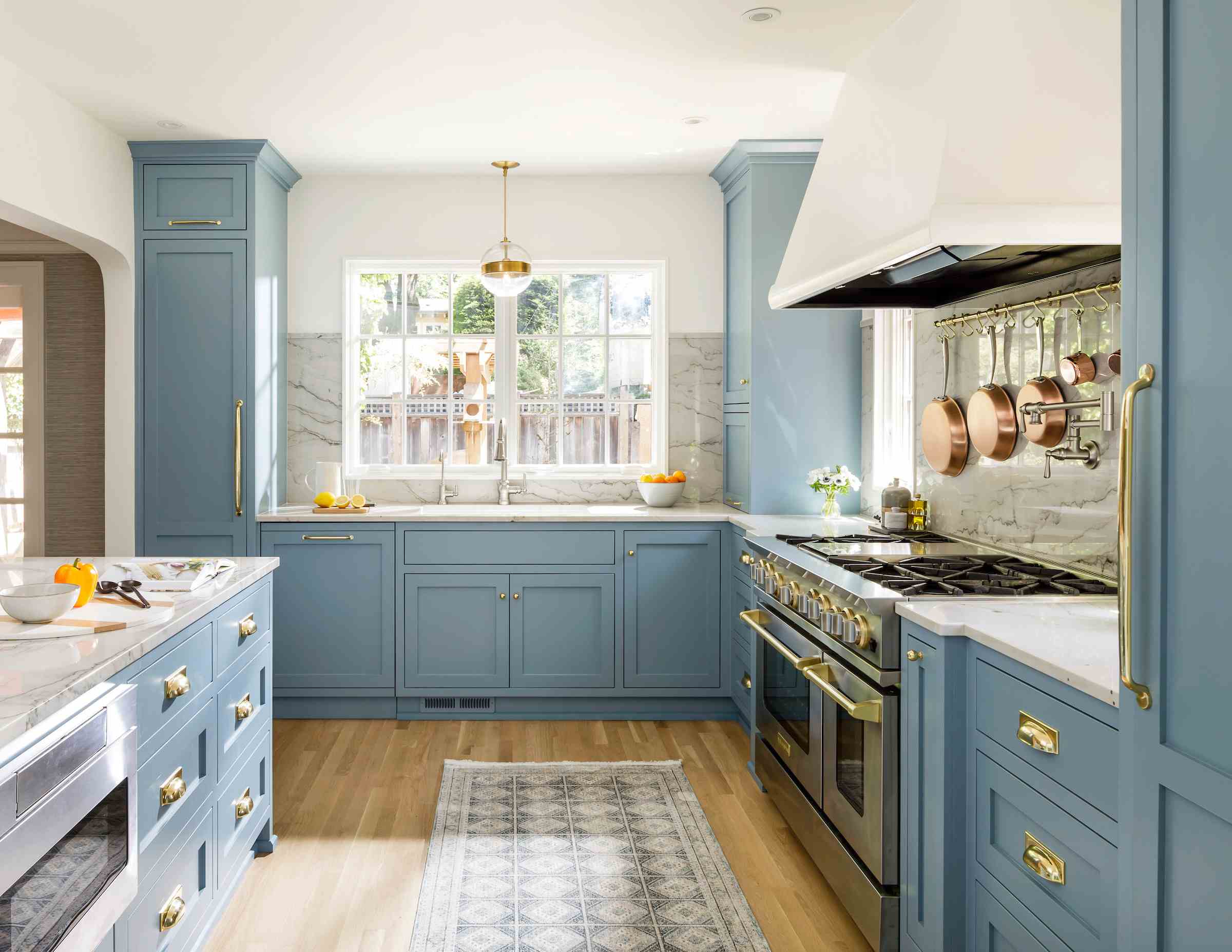 blue kitchen with kitchen island, rug, wooden floors, sink, silver appliances, countertops and chimney