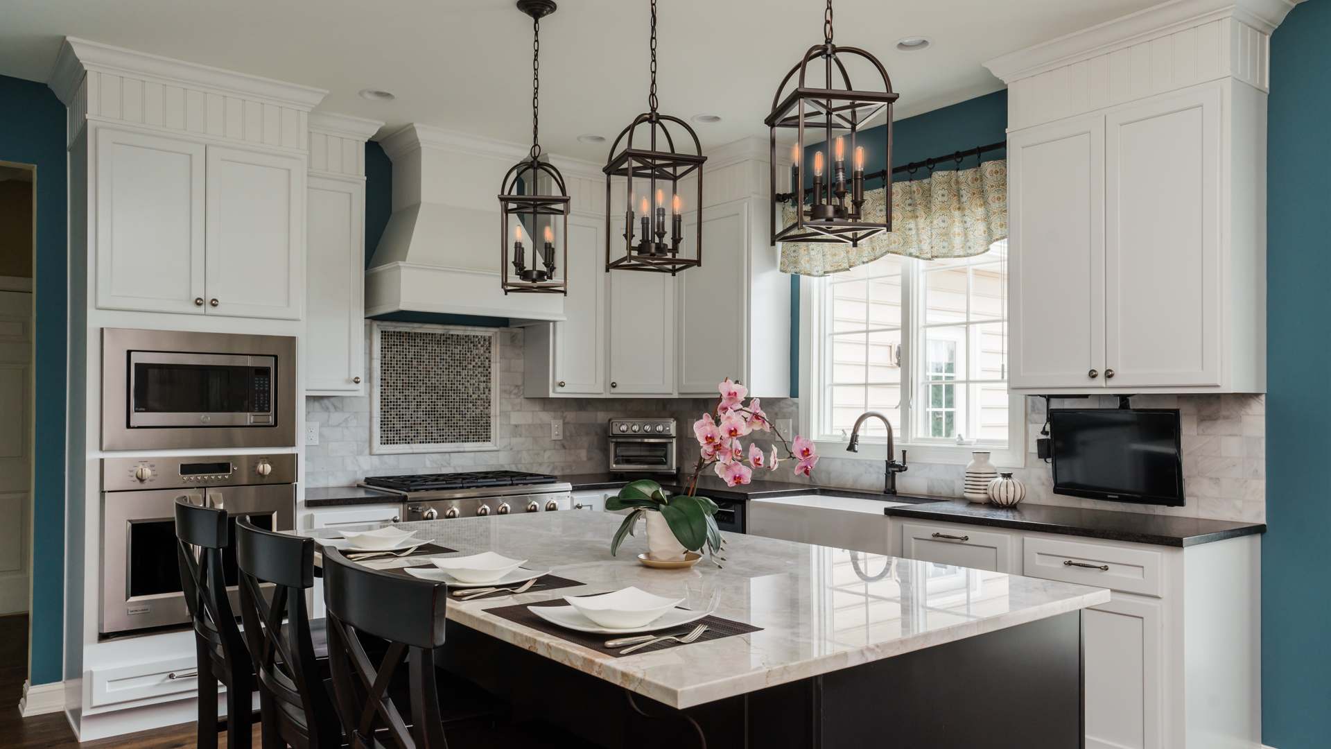 white kitchen with hanging lights, kitchen island, sink, white and black marble countertops and appliances