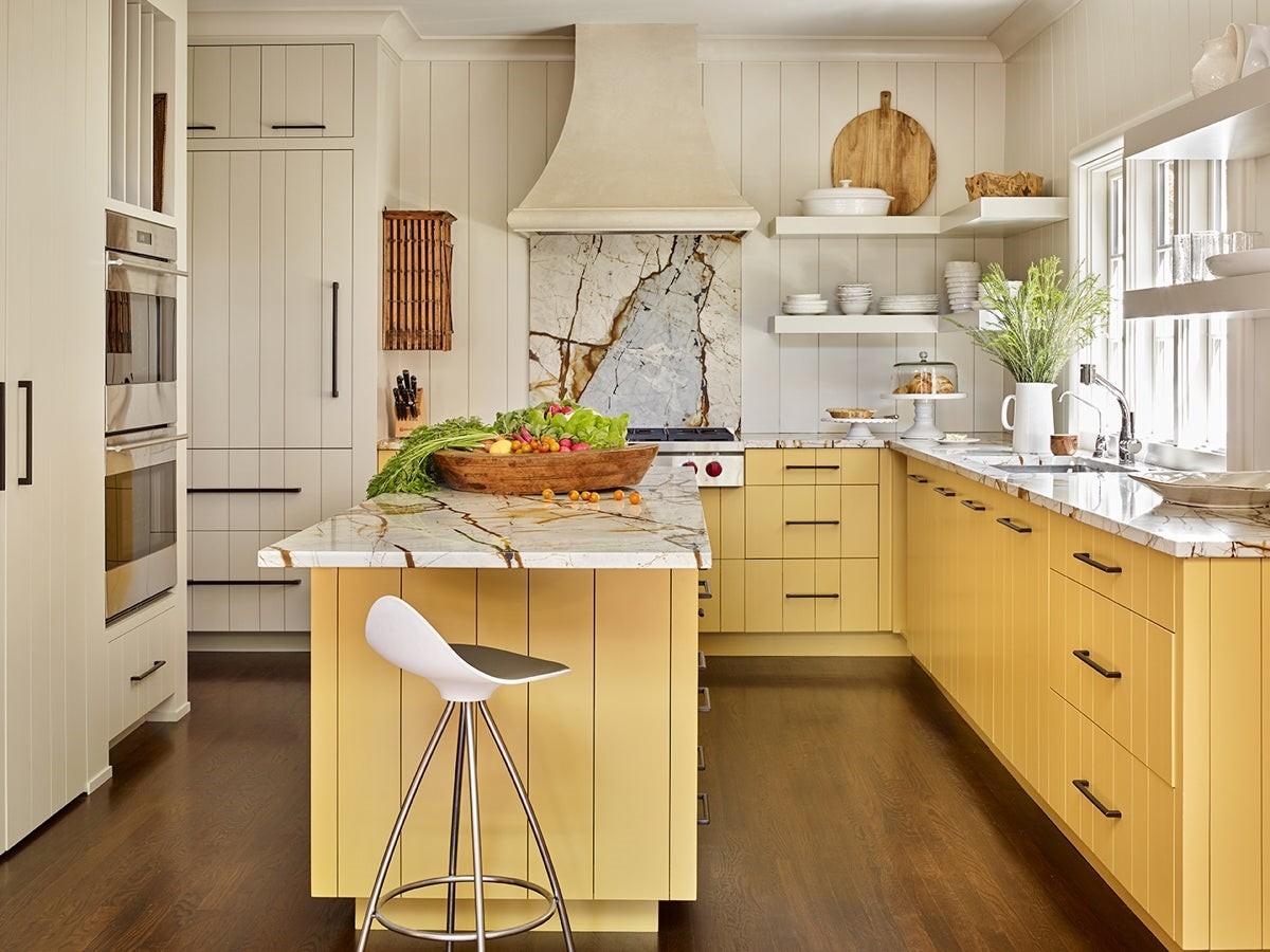 yellow kitchen cabinets with white marble countertops, chimney, sink, shelves, plants, cupboard and chair