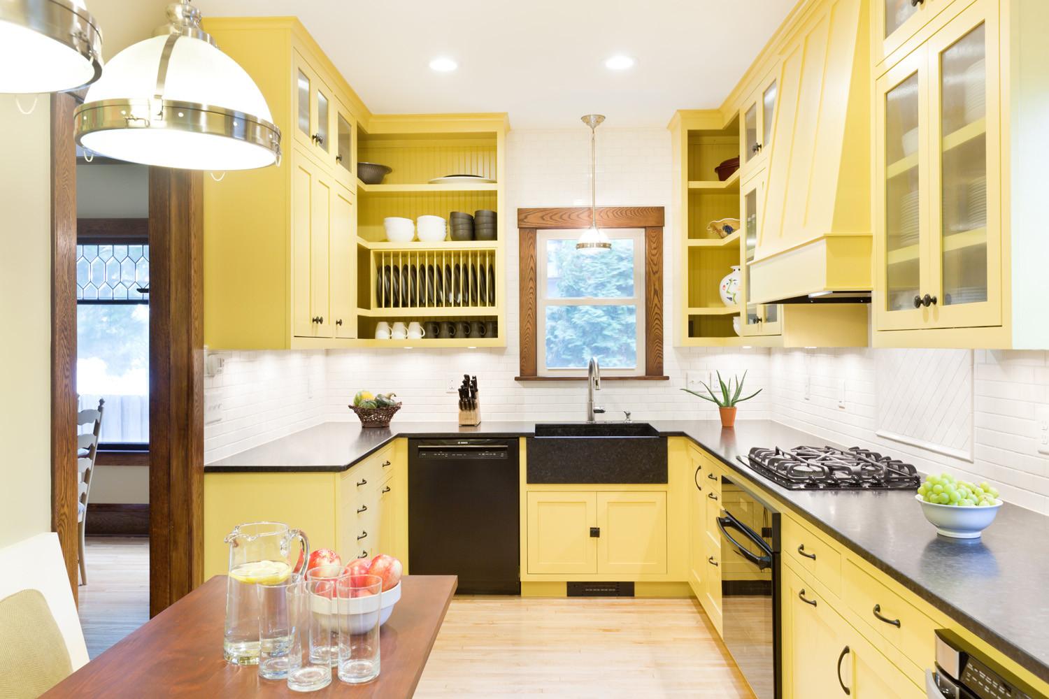 yellow kitchen cabinets with black appliances, sink, table, and black countertops,