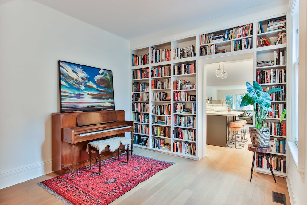 wall covered with a bookshelf, designer rug on floor, wood flooring, painting hanging on wall, chair, hall decor