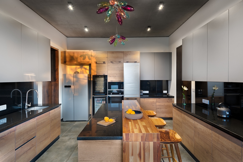 modern luxury kitchen by Keystone architects, kitchen design with stainless steel appliances, black built-in appliances, wood cabinets, granite countertop, wooden island and an eccentric chandelier