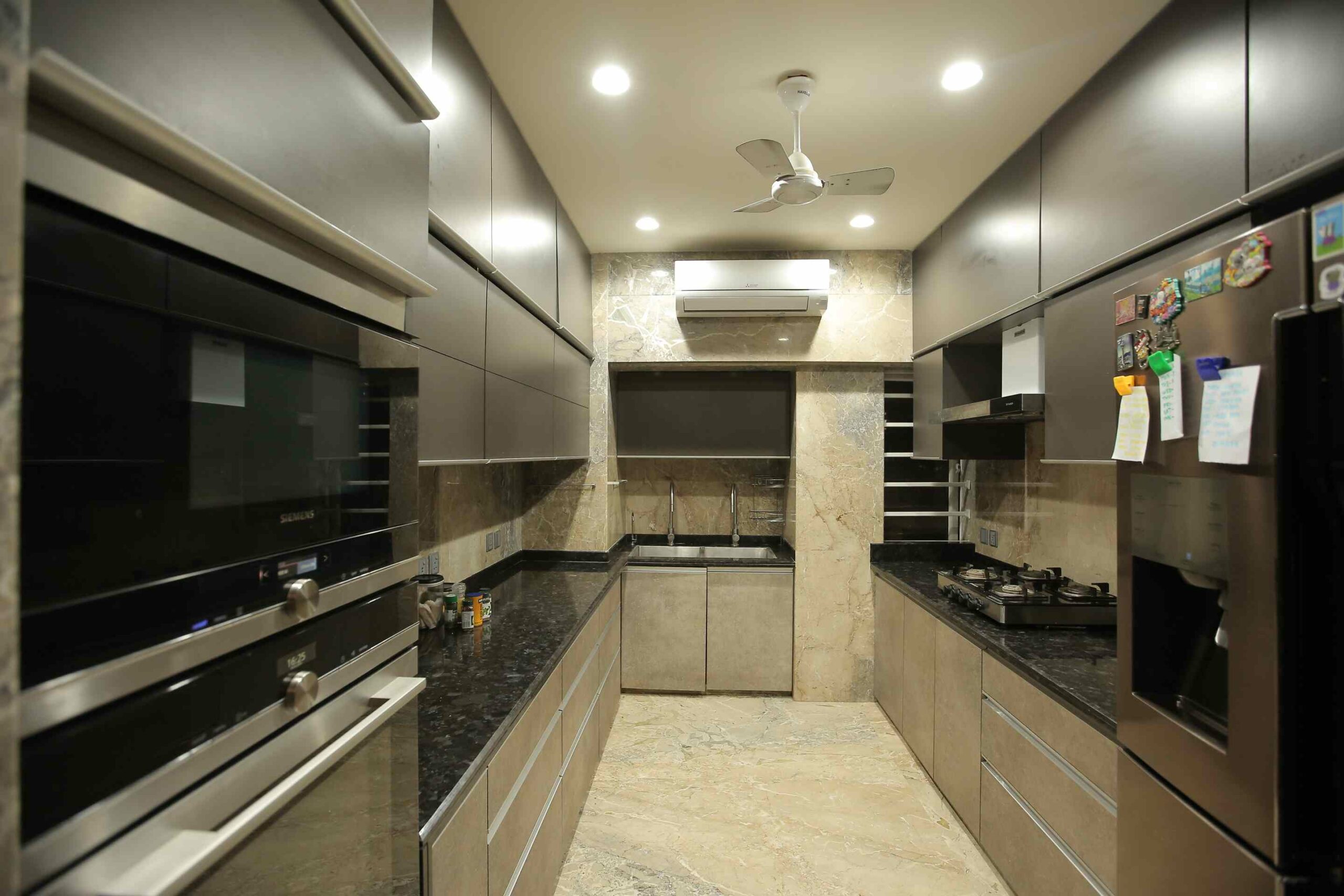 silver kitchen cabinets with black appliances, fan, sink, and AC, smart automated home appliances in a high end kitchen design by interior designer Vandana Buddhia or Vermillion