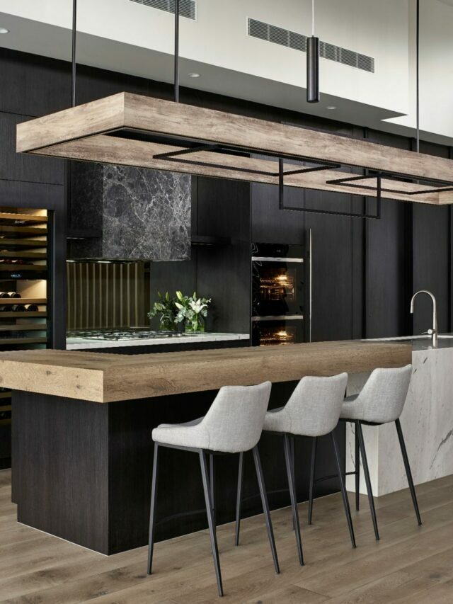 black kitchen with brown kitchen islands, chandelier, white chairs and appliances