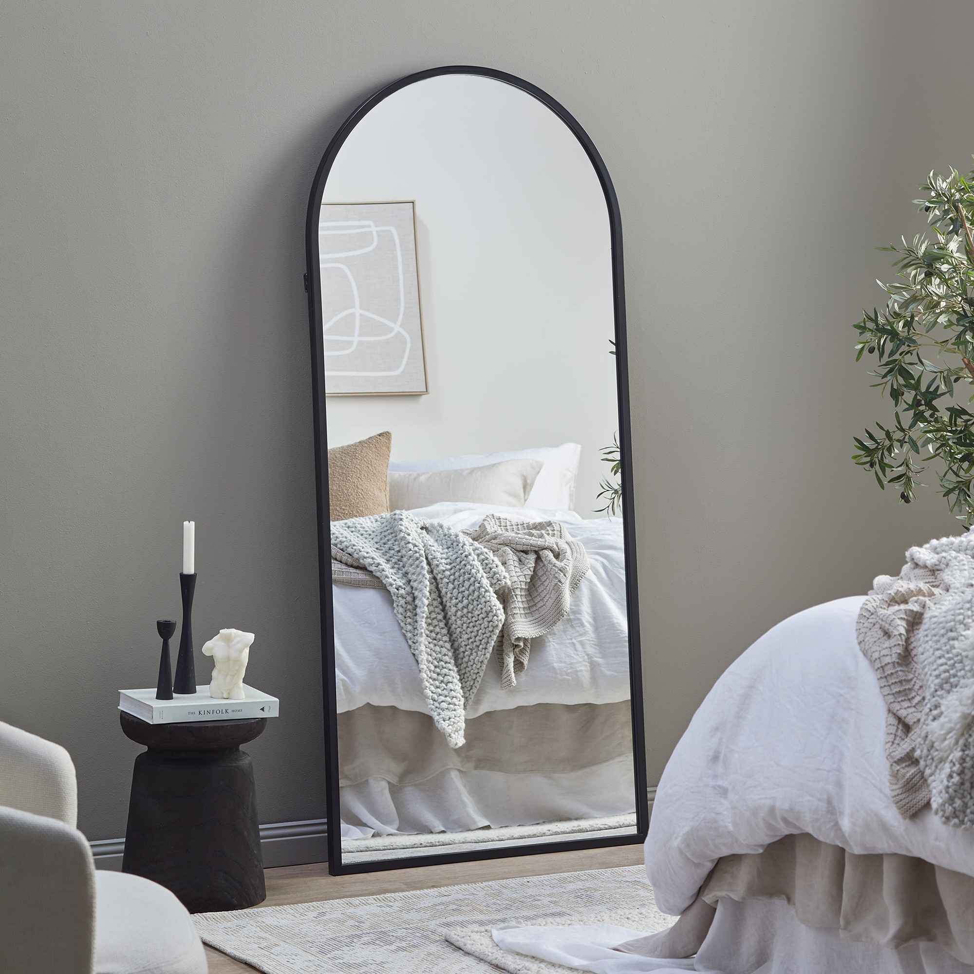 mirror in a bedroom with black side table, bed, indoor plants, candles and chair