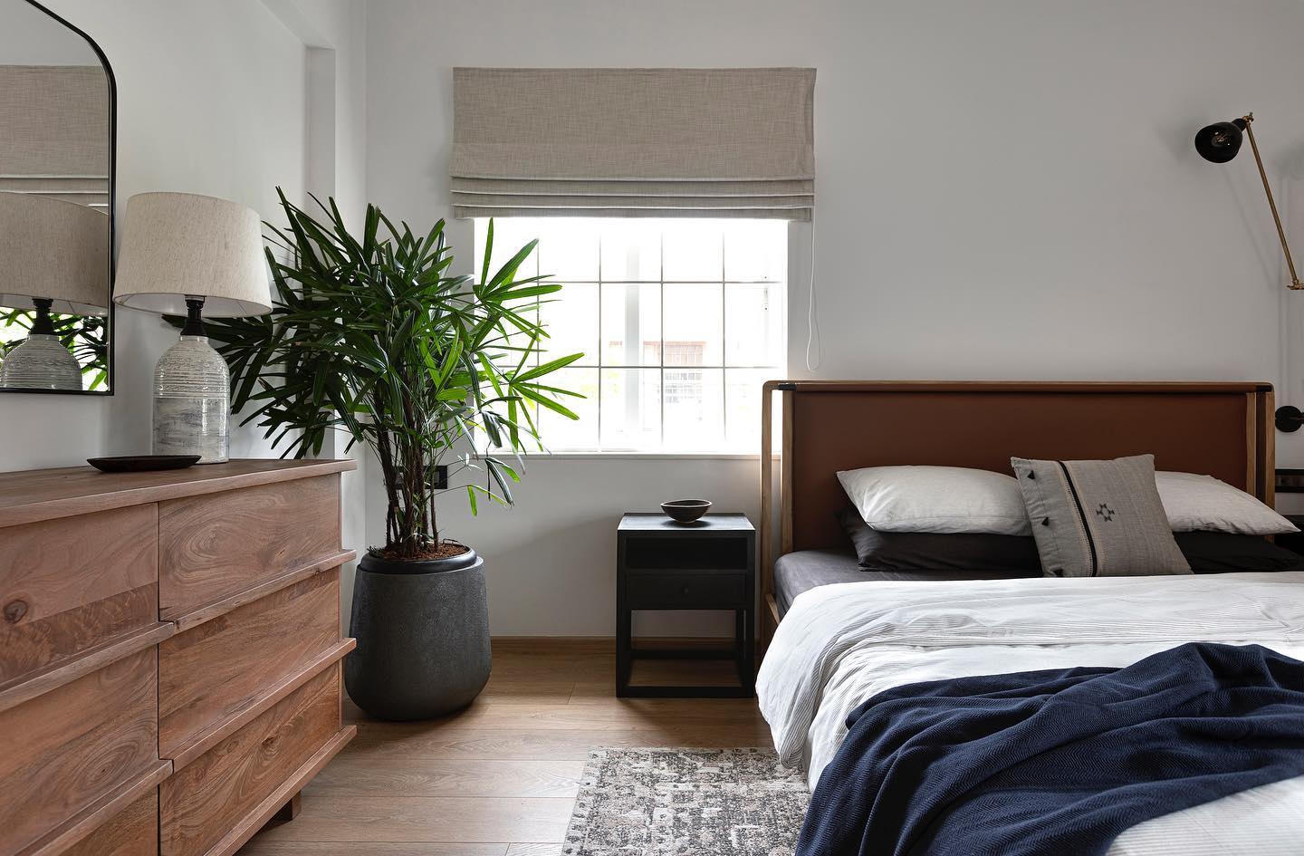 indoor plant in a black pot in a bedroom with bed, rug, brown cabinet and a black table
