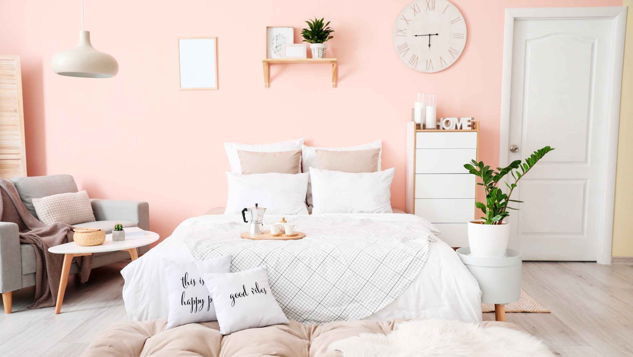 peach bedroom with white bed, grey chair, white cabinet, plants and pendant light