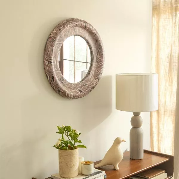 mirror design with frame, round shape, hanged over a wooden table, lamp with white shade on the table, decor pieces on the table