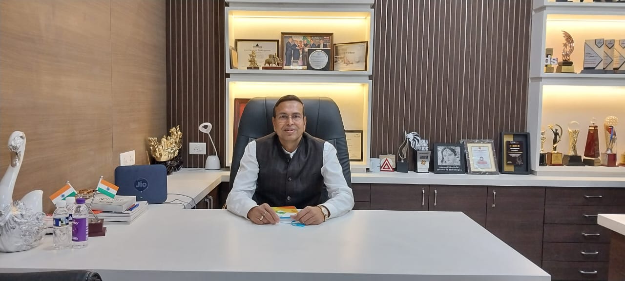 Mr. Jagdish Agarwal sanitaryware, bathroom fittings and stiebel eltron dealers in Guwahati sitting in his office with a white desk, chair, awards and decorative items