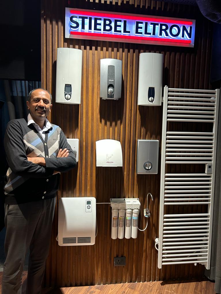 Mr. Pankaj Jain of Stylish Baths a bathroom fittings and sanitary ware dealer in Ludhiana standing in front of Stiebel Eltron brown display wall at a showroom