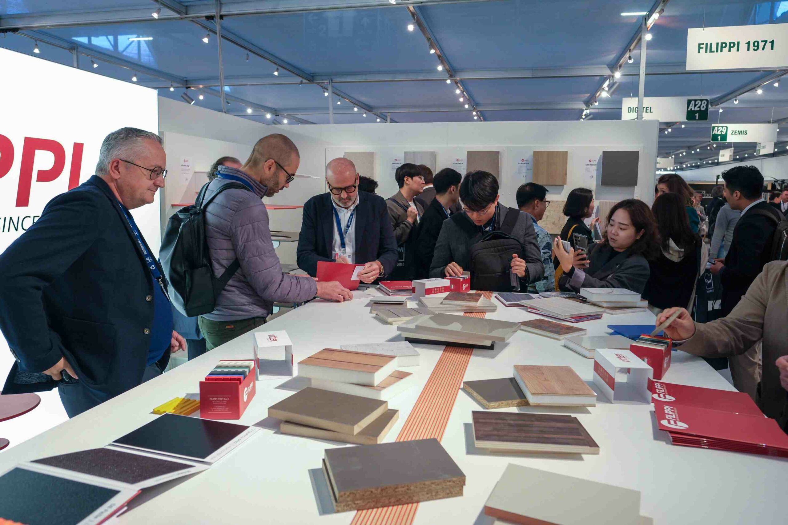 a crowd gathered around a white table examining samples at SICAM Pordenone furniture fair 2023